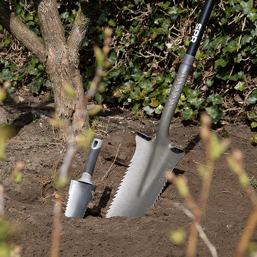 Zaagspade en mini wortelzaag staan samen in een plantgat bij een boom