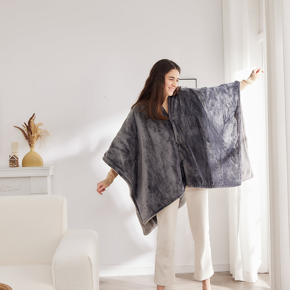 Vrouw staat in de woonkamer met de grijze elektrische poncho om en haar armen gespreid