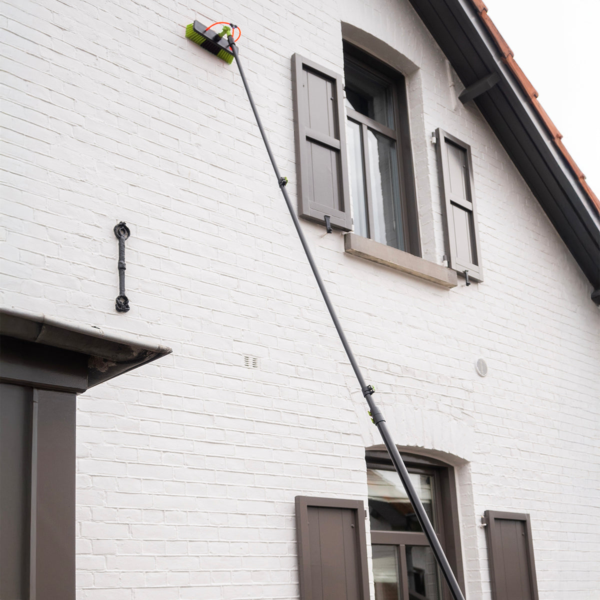 Uitgeschoven wasborstel reinigt de gevel van een wit huis tot aan de dakgoot