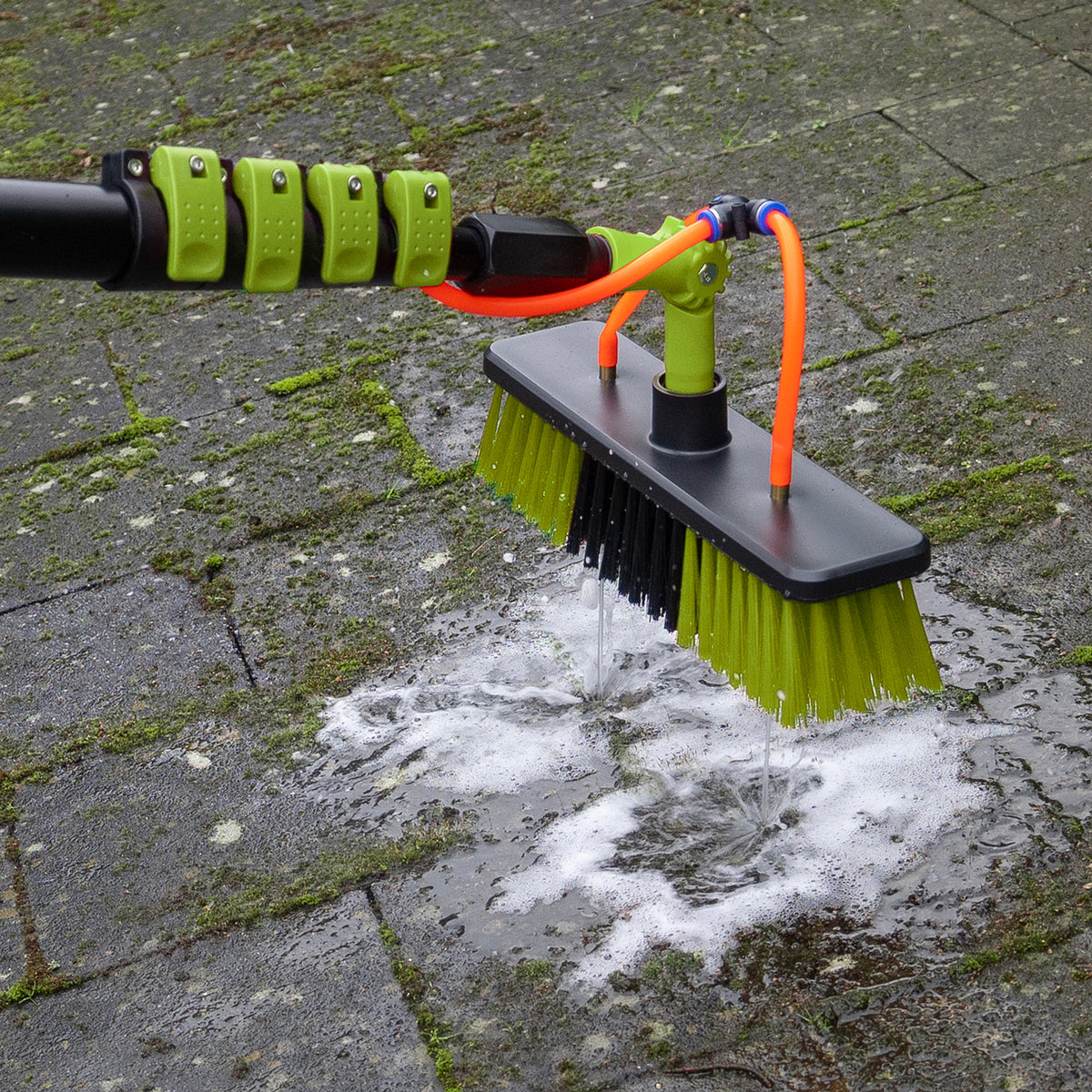 Wasborstel schrobt terrastegels met groene aanslag schoon met zeepschuim