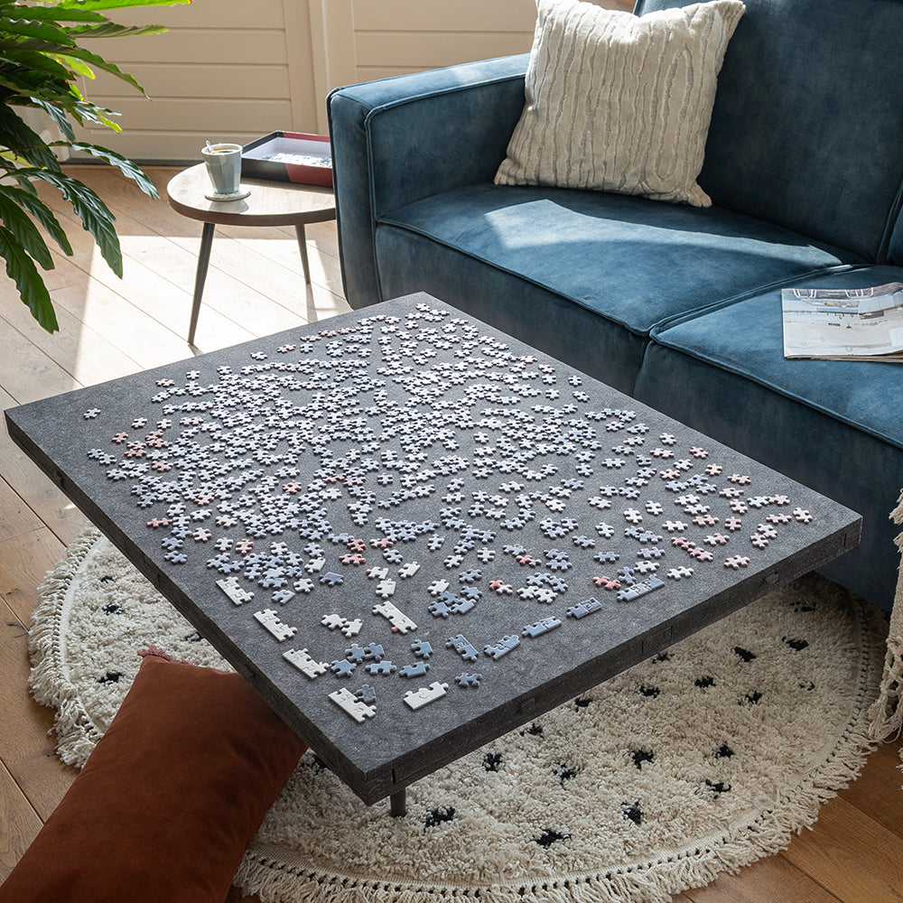 Grand plateau de puzzle en feutre couvert de pièces sur une table basse, tiroirs fermés
