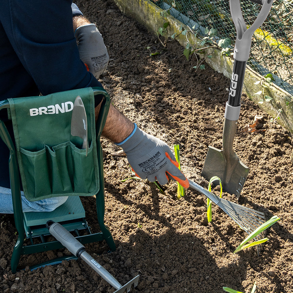 Une personne assise sur un tabouret de jardin travaille avec la griffe entre de jeunes plants, la bêche plantée dans le sol