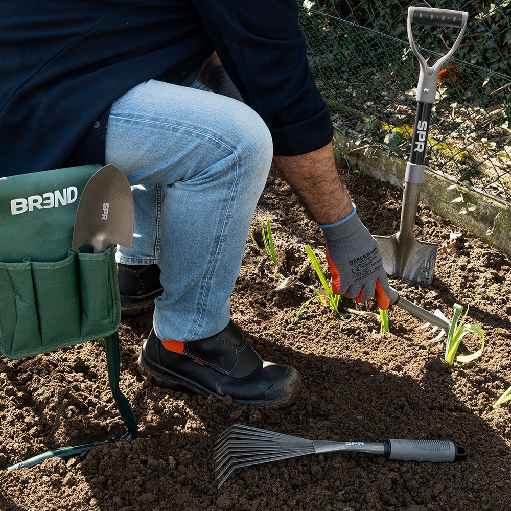 Un homme sur le tabouret de jardin travaille au potager, avec le mini-râteau à feuilles et la bêche à côté de lui