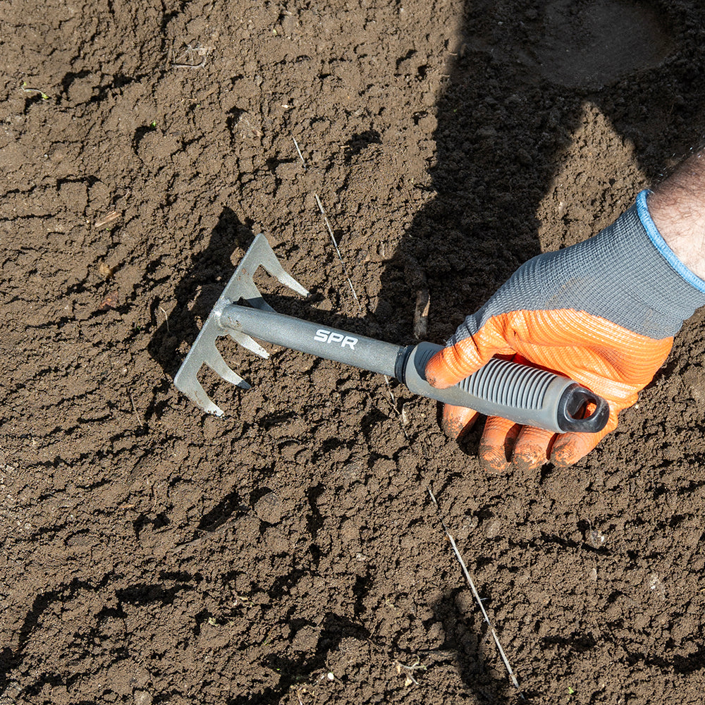 Une main ameublit la terre avec la griffe à 5 dents
